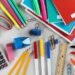 Promotional graphic featuring assorted back-to-school supplies including notebooks, pencils, pens, markers, folders, and classroom essentials.