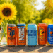 A vibrant summer-themed photo showcasing five colorful energy drink cans from brands like Monster and Reign, arranged on a sunlit outdoor table with a vase of bright sunflowers in the background.
