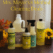 Mrs. Meyer’s and Method cleaning products arranged with fall leaves and candles in a cozy kitchen scene.