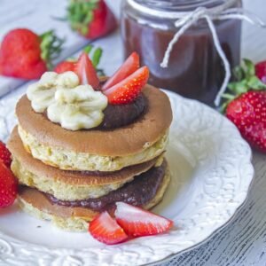 Stack of layered pancakes topped with berries and whipped chocolate on a rustic breakfast table