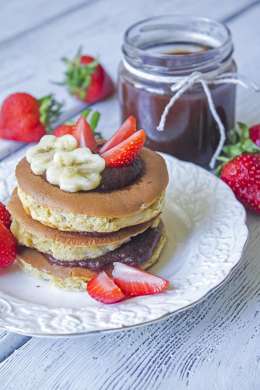 Stack of layered pancakes topped with berries and whipped chocolate on a rustic breakfast table