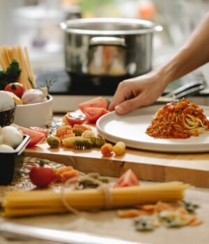 A close-up of spaghetti pasta in a kitchen setting with a soft blue sky-inspired background, light cloud textures, and delicate cherry blossom accents creating an airy spring cooking scene.