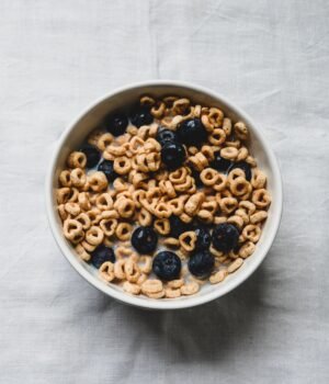 A cozy breakfast scene featuring a bowl of cereal with fresh blueberries on a linen tablecloth with soft natural spring lighting