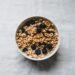 A cozy breakfast scene featuring a bowl of cereal with fresh blueberries on a linen tablecloth with soft natural spring lighting