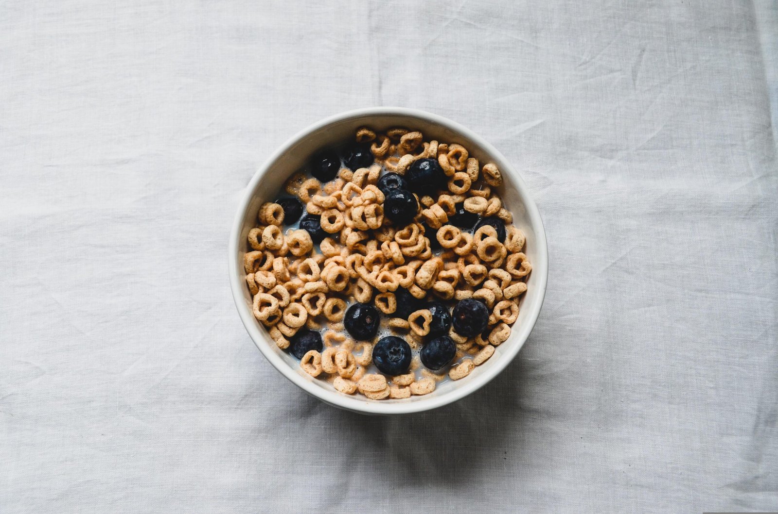 A bright spring-themed breakfast pantry setup featuring cereal bowls, blueberries, snack foods, and baking mixes with soft blue skies, light clouds, and subtle cherry blossom accents for a cozy seasonal feel