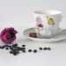 A cozy spring-themed coffee setup featuring coffee mugs and pods with soft blue skies, light clouds, and subtle cherry blossom accents for a calm seasonal feel
