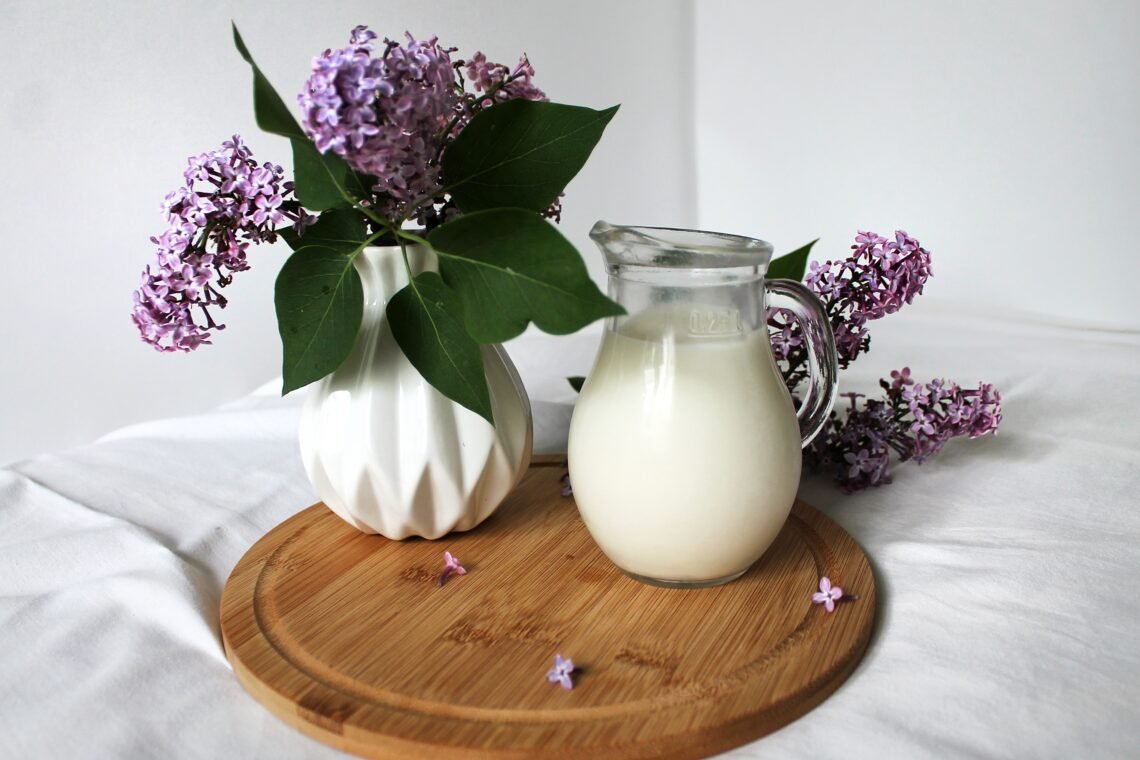 A soft spring-themed pantry beverage setup featuring milk cartons with light clouds, soft blue skies, and subtle cherry blossom accents for a calm seasonal feel