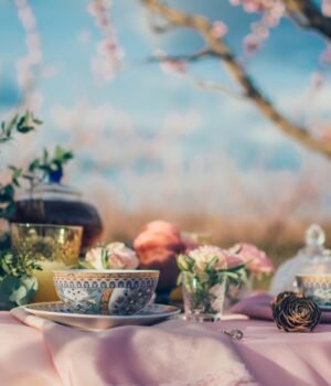 A cozy spring-themed tea setup featuring tea cups and beverage products with soft blue skies, light clouds, and subtle cherry blossom accents for a calm seasonal feel