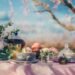 A cozy spring-themed tea setup featuring tea cups and beverage products with soft blue skies, light clouds, and subtle cherry blossom accents for a calm seasonal feel