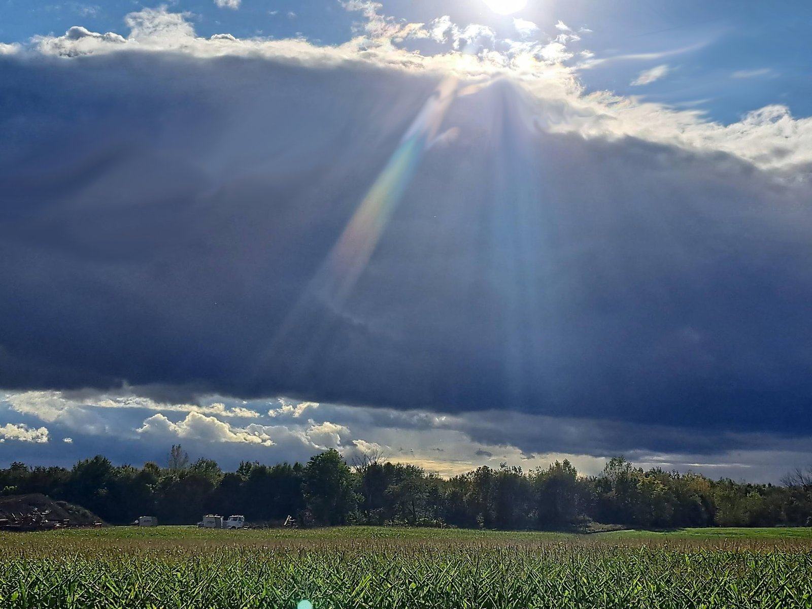 Sunlight breaking through dramatic clouds over a rural farm field.
